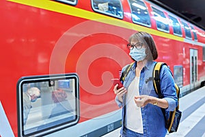 Woman passenger in medical face mask waiting on railway platform inside station