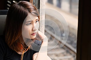 Woman passenger sitting inside train and looking through window. Teenage girl with orange headset feels lonely and looking