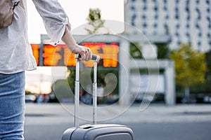 Woman passenger with suitcase is checking arrival and departure board schedule timetable at train or bus station