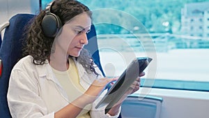 Woman passenger using tablet PC and listening to music in train