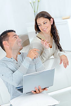 Woman passing credit card to partnet using laptop