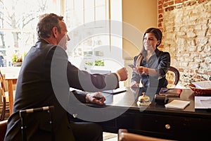 Woman passing room key to a guest at check-in desk of hotel