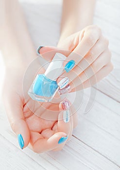 Woman with pastel manicure holding blue nail polish. Skin treatment and body care concept.