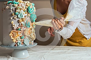 Woman pastry chef decorating a cake with a pastry bag with cream