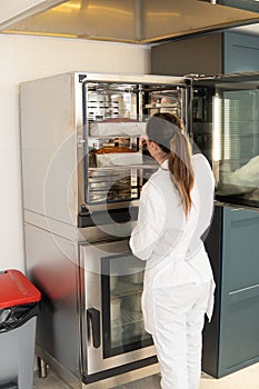 woman pastry chef uniformed in white takes out two sponge cakes that are inside an industrial oven. workplace Professional bakery