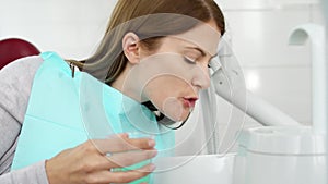 Woman patient in dental clinic. Rinsing out after teeth treatment. Dental equipment on background