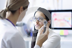 Woman patient holding ear near doctor with otoscope in hand in clinic