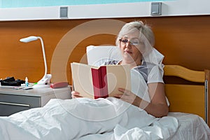 Woman patient is reading a book, while lying in the hospital bed