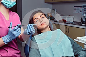 Woman patient sitting in a dentist chair while her doctor preparing for syringe injection.
