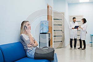 Woman patient in speaking at the mobile phone in hospital waiting room.