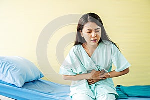 Woman patient  suffering from stomach ache while sitting on bed at hospital, abdominal pain, food poisoning photo