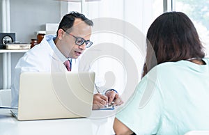 Woman patient visiting Indian male doctor at clinic office. Medical worker wear glasses giving healthcare consultation to Asian