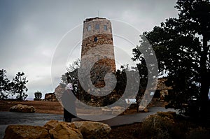 A woman pauses on the path to observe the watch tower in the Grand Canyon on a cold blustery day