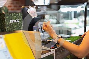 Woman paying bill through smartwatch using NFC technology in cafe.