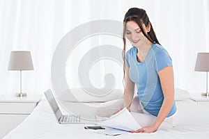 Woman paying her bills online with laptop in bedroom