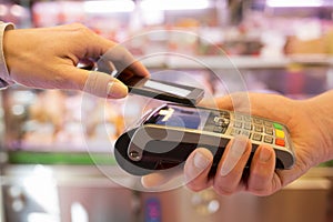 Woman paying with NFC technology on mobile phone, in supermarket