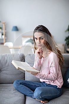 Woman peacefully reading a book on living room sofa. Domestic life