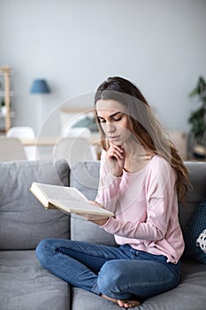 Woman peacefully reading a book on living room sofa. Domestic life