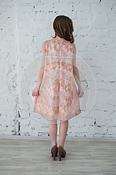 Woman in a peach dress against the white brick wall