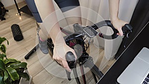 Woman is pedaling out of saddle on stationary bicycle simulator. Indoor cycling