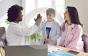 Woman pediatrician high fives a happy little boy who came to the clinic with his mother