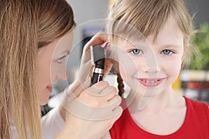Woman pediatrician looking at eardrum of little girl using otoscope in clinic photo