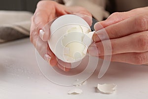 Woman peeling boiled egg at white wooden table, closeup