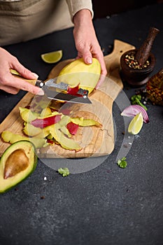 Woman peeling mango on a wooden cutting board at domestic kitchen
