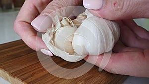 Woman peeling off skin from garlic clove on wooden tabletop. Slow mo Close up