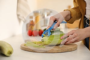 Woman peeling zucchini at kitchen counter, closeup. Preparing vegetable