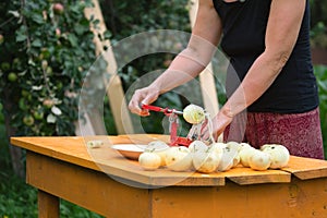 Woman peels apples using an apple peeler device on the orange table in the garden