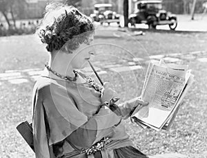 Woman with a pencil in her mouth reading the newspaper