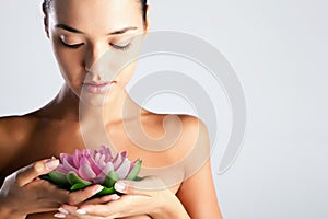 Woman with perfect spotless skin holds a lotus flower spa skincare nude shoulders