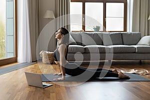 Woman perform Upward Facing Dog asana near opened laptop