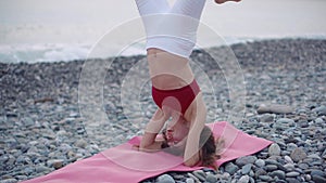 Woman is performing headstand on pebble beach near sea, hatha yoga practice