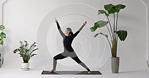 Woman performing Virabhadrasana exercise, warrior pose number one and two, training in black sports overalls