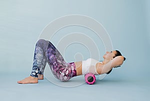 Woman performs myofascial relaxation of the hyperflexible muscles of the back with a massage roller on a blue background. The