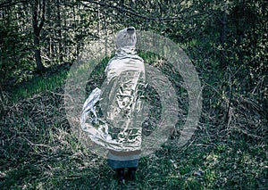 Woman person is lost and stand in wild forest in cold day, using first aid emergency blanket to prevent hypothermia and body heat