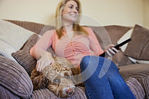 Woman With Pet Cockapoo Dog Relaxing On Sofa Watching TV At Home