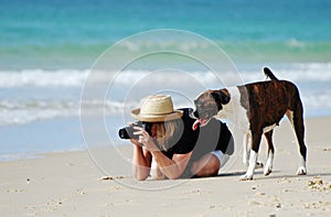 Woman & pet dog on tropical beach taking photos