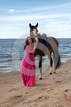 a woman pets the horse on a beach near the ocean