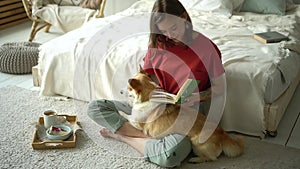 Woman petting dog on her knees while educating, reading book Avki. female sit on floor busy