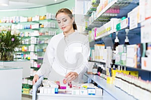 Woman pharmacist is searching medicines on shelves in medical shop