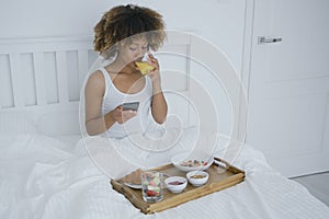Woman with phone enjoyin breakfast in bed
