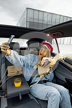 Woman with phone and flowers on backseat of a car