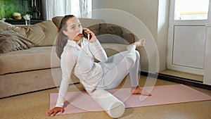 Woman with phone massages back with roller on pink mat