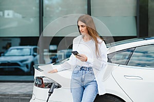 Woman with phone near an rental electric car. Vehicle charged at the charging station