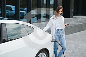 Woman with phone near an rental electric car. Vehicle charged at the charging station