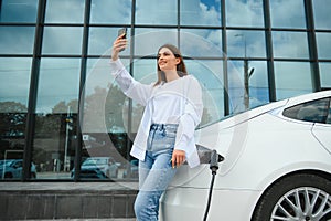 Woman with phone near an rental electric car. Vehicle charged at the charging station