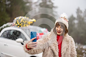 Woman with phone traveling by car decorated for Christmas in mountains